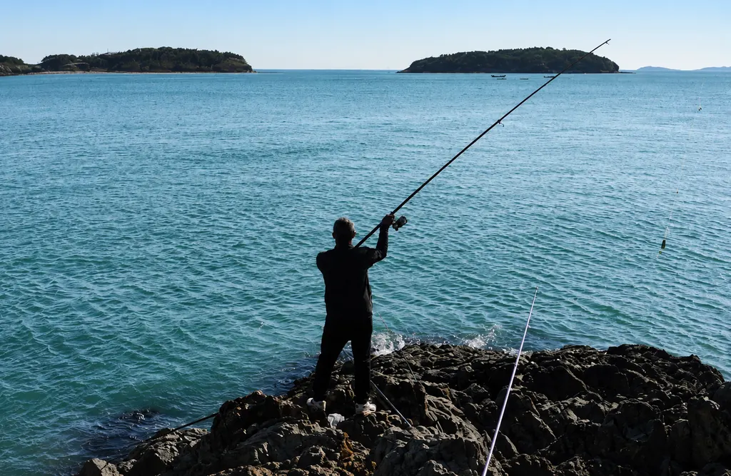 An angler casting from the rocks at a river estuary, reaching the deeper water.